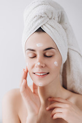 Young happy woman wrapped with bath towel applying  cream to her face for skin care. Skin care concept. Skin care and beauty concept. Place for text 