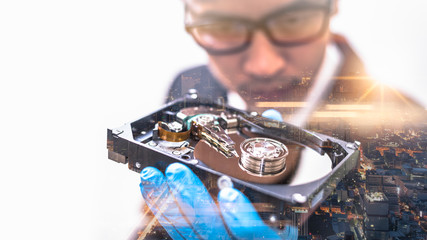 the double exposure image of the businessman hold and looking to inside of hard disk drive overlay with cityscape image. the concept of technology, data and business.