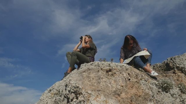 Young women travelers with map looking far away through binoculars