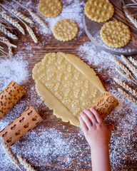 The child rolls out the dough for cookies with a wooden rolling pin. Children's hand in the frame
