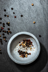 Black pepper in small bowl for spices on dark background. Bowl with text Pepper on the bottom.