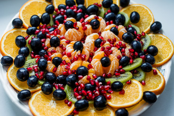 Fruit dessert. Orange, grapes, pomegranate on a white plate. Festive table.