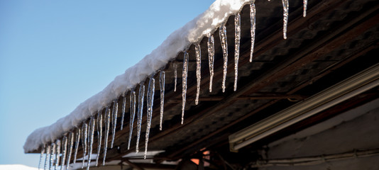 stalactite ice hangs from the roof of the house winter background