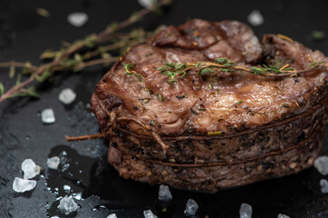 Grilled piece of beef with thyme and salt on a black background.