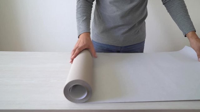 handyman preparing new wallpaper roll for marking on table indoor