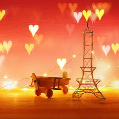 Valentine's day background. Eiffel tower and wooden toy plane, over the table and red bakground. Hearts overlay.