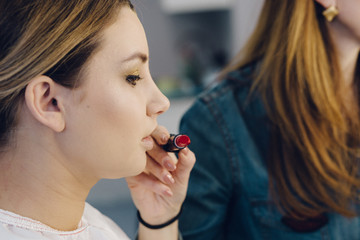 Closeup makeup artist applying red lipstick on model's lips working in beauty salon. Closeup view of an artist's hand selects the color of lipstick