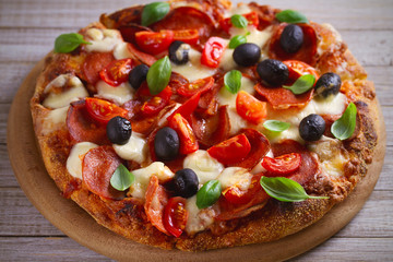  Pizza with pepperoni, tomatoes, cheese, olives and basil. Delicious pizza served on wooden plate on rustic background. horizontal
