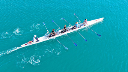 Aerial drone bird's eye top view of sport canoe operated by team of young women in emerald clear sea