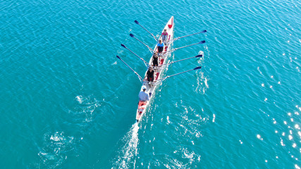 Aerial drone bird's eye view of sport canoe operated by team of young women in emerald clear sea