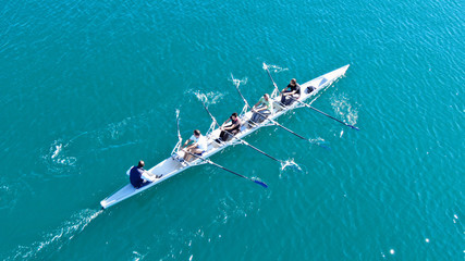 Aerial drone bird's eye view of sport canoe operated by team of young women in emerald clear sea