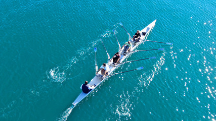 Aerial drone bird's eye view of sport canoe operated by team of young women in emerald clear sea