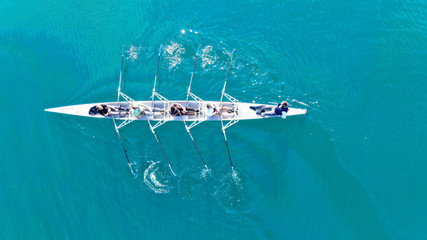 Aerial drone bird's eye top view of sport canoe operated by team of young women in emerald clear sea