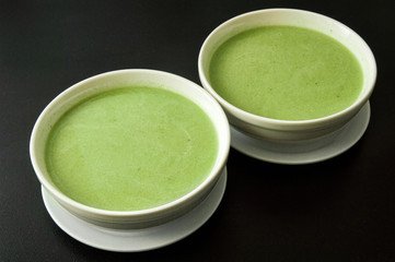 Close up. Two round white plate filled with green broccoli cream soup. Black background. Copy space.