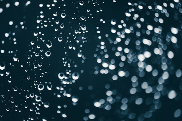 Dirty window glass with drops of rain. Atmospheric blue background with raindrops in bokeh. Droplets and stains close up. Detailed transparent texture in macro with copy space. Rainy weather.