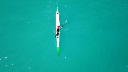 Aerial drone bird's eye view of sport canoe operated by young fit man in emerald clear waters