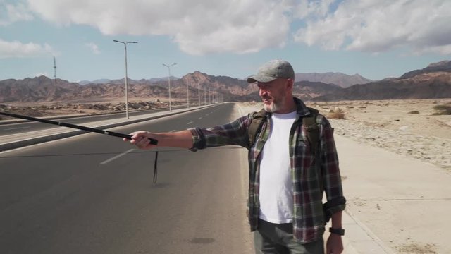 Hand-held shot of senior traveler male shooting himself with monopod
