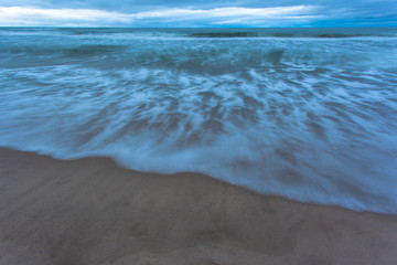 waves and tide on the sea at a sandy beach during blue twilight in cloudy weather on a long exposure