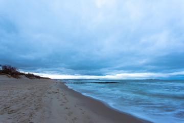 sandy beach with a breakwater by the cold sea during blue twilight in cloudy weather on a long exposure