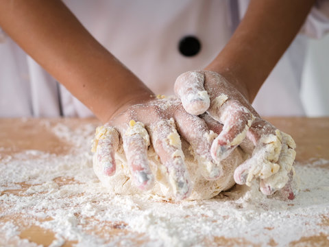 Kid hands in uniform preparing dough for pizza or bread, lifestyle concept.