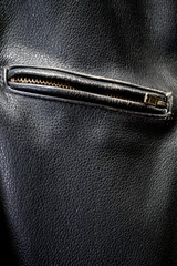 Close up of old black leather motorcycle jacket focusing on zippered pocket.