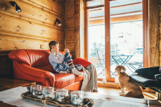 Boy sitting on cozy couch at living room and his beagle dog watching in wide window in cozy home atmosphere. Peaceful moments of cozy home concept image.
