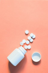 white pills scattered on a pink background. pills spilled out of the bottle. copy space for text