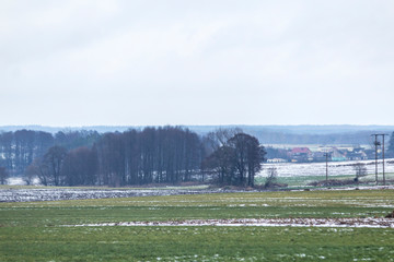 A bit of snow on the plowed field. Village and forest in the background. The beginning of winter in Europe.