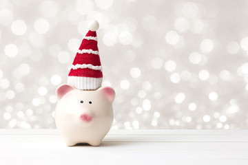 Piggy bank and santa claus hat over white wooden table abstract bokeh light background with copy space. Saving and christmas holiday concept.