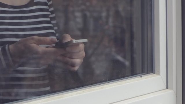 Woman using mobile phone for text messaging by the window