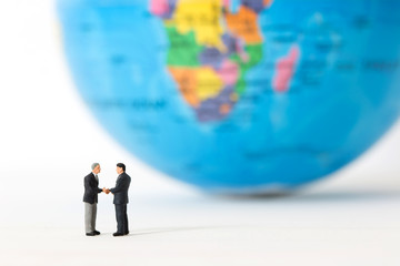 Miniature businessmen shaking hands  on blurred global or world background. Concept of partnership. Business successful.