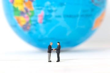 Miniature businessmen shaking hands  on blurred global or world background. Concept of partnership. Business successful.
