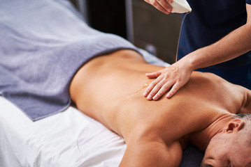 Masseur pouring massage oil on her hand and client back