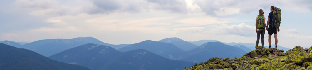 Back view of young tourist couple with backpacks, athletic man and slim girl stand holding hands on...