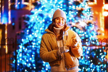 Beautiful girl or woman with a glass of champagne and sparkle in the open air on the background of christmas tree in a winter