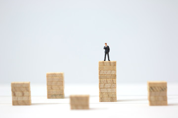 Miniature businessman making the decision on highest wooden stacks. Business goal achievement concept.
