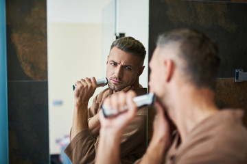 Attractive serious man looking in the mirror and shaving