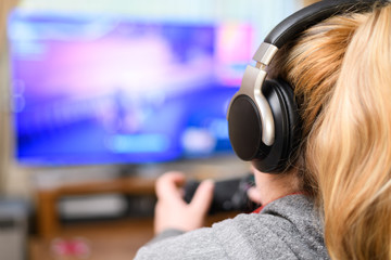 Rear View Of An Girl Playing Video Games At Home, wearing wireless headphones