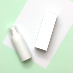 White cosmetic products and pink tulip flower on mint green and white paper background. Natural beauty products for branding mock-up concept.