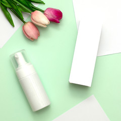 White cosmetic products and pink tulip flower on mint green and white paper background. Natural beauty products for branding mock-up concept.