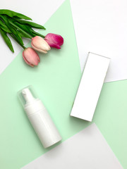 White cosmetic products and pink tulip flower on mint green and white paper background. Natural beauty products for branding mock-up concept.