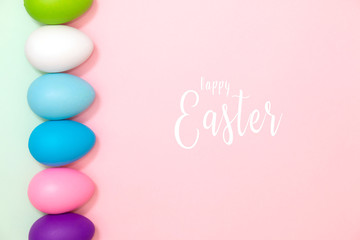 Flat lay of colorful easter eggs on pastel pink and green background with text Happy Easter. Minimal style.