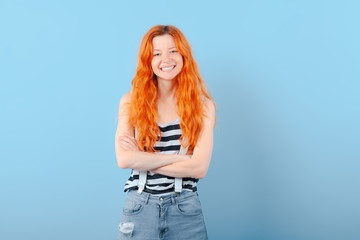 Red-haired girl smiles, having combined hands on breast on blue background