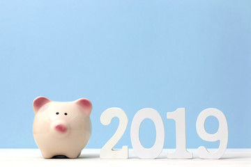 Pink piggy bank with wooden white number 2019 on table and blue soft pastel background. Happy New Year 2019 financial concept.
