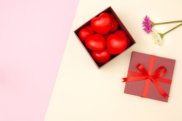 Flat lay of red heart in gift box and flowers on pink and yellow pastel background with copy space. Love and Valentine's day concept. Minimal style.