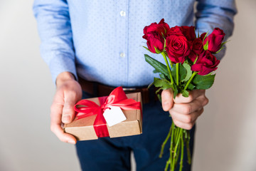 Valentines day,man holding red roses and gift with bow and tag,romantic surprise.