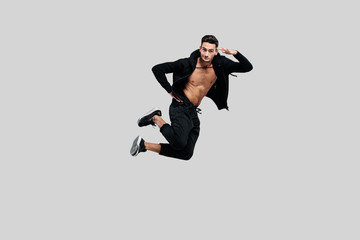 Fototapeta na wymiar Handsome young dancer of street dancing dressed in black pants and a sweatshirt on a naked torso jumps on a white background