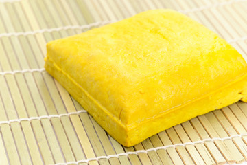 Yellow tofu loaf on bamboo sheet.