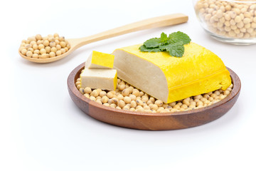 Yellow tofu loaf in a wooden tray filled with soy. and Some pieces are cut.