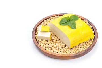 Yellow tofu loaf in a wooden tray filled with soy. and Some pieces are cut.